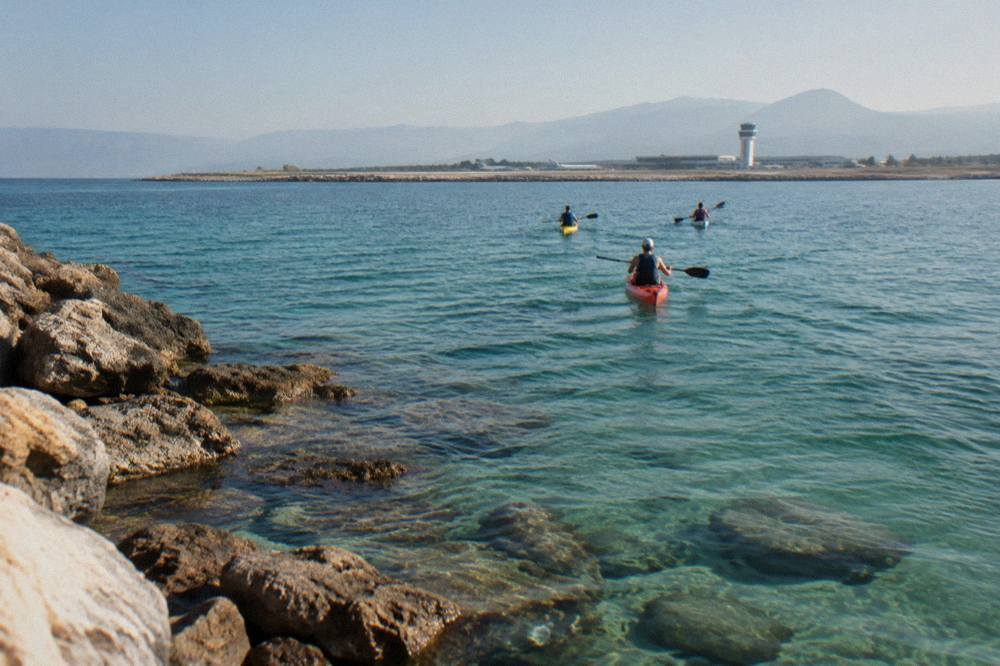 Kayakers paddling over clear green water near a rocky shore