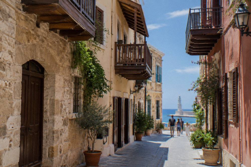 A narrow stone lane in Chania Old Town with wooden balconies and a few pedestrians