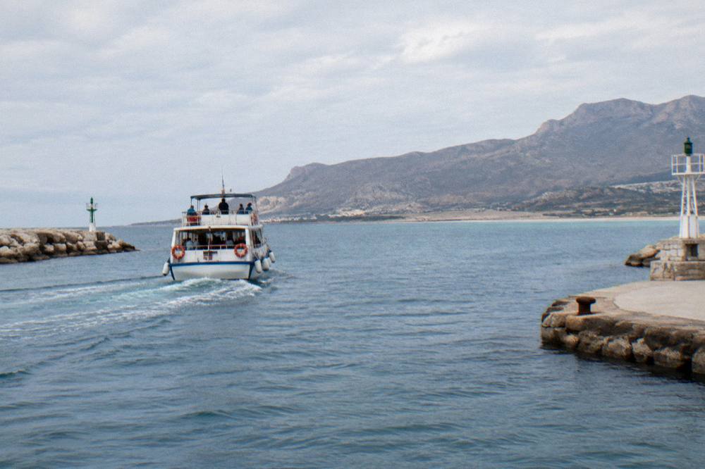 An excursion boat departing Kissamos port toward a lagoon on a clear morning