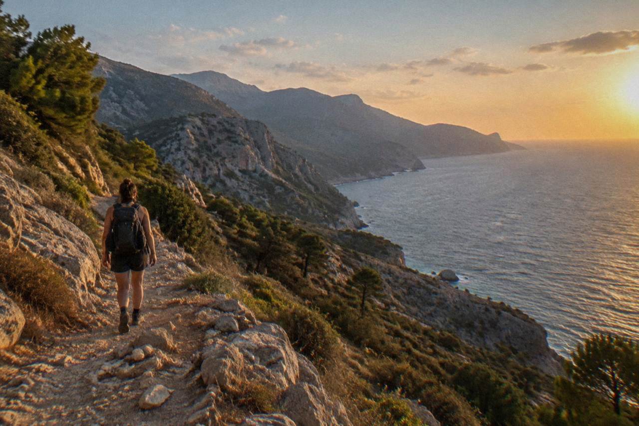 A hiker with a backpack walking a rocky trail above the sea in western Crete