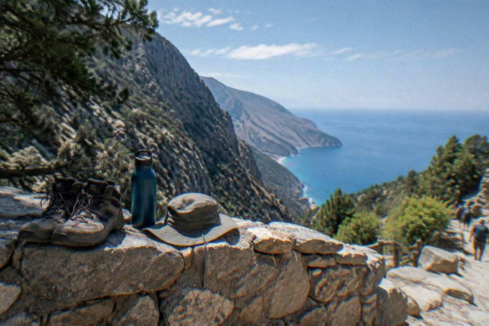 Hiking boots, a water bottle and a hat resting on a stone wall above the sea