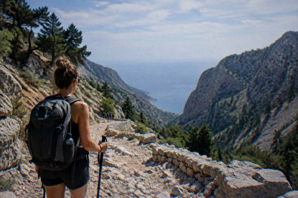 A hiker looking out over a rocky mountain road toward the sea at midday