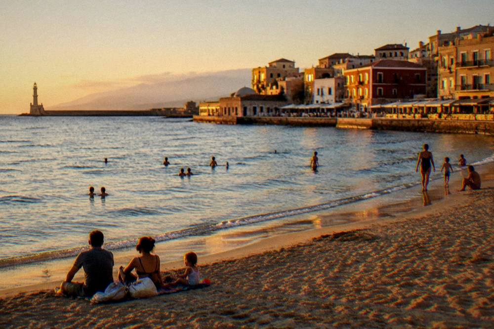 Families and swimmers on a calm sandy beach near Chania in late afternoon light