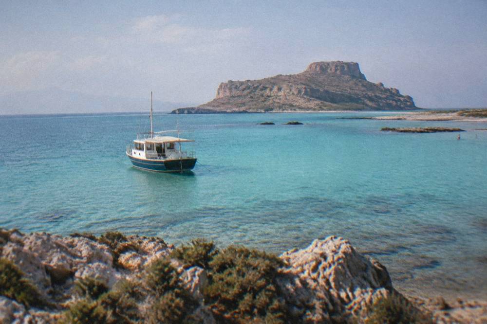 Boat anchored in the turquoise shallows of Balos Lagoon with Gramvousa island in the distance