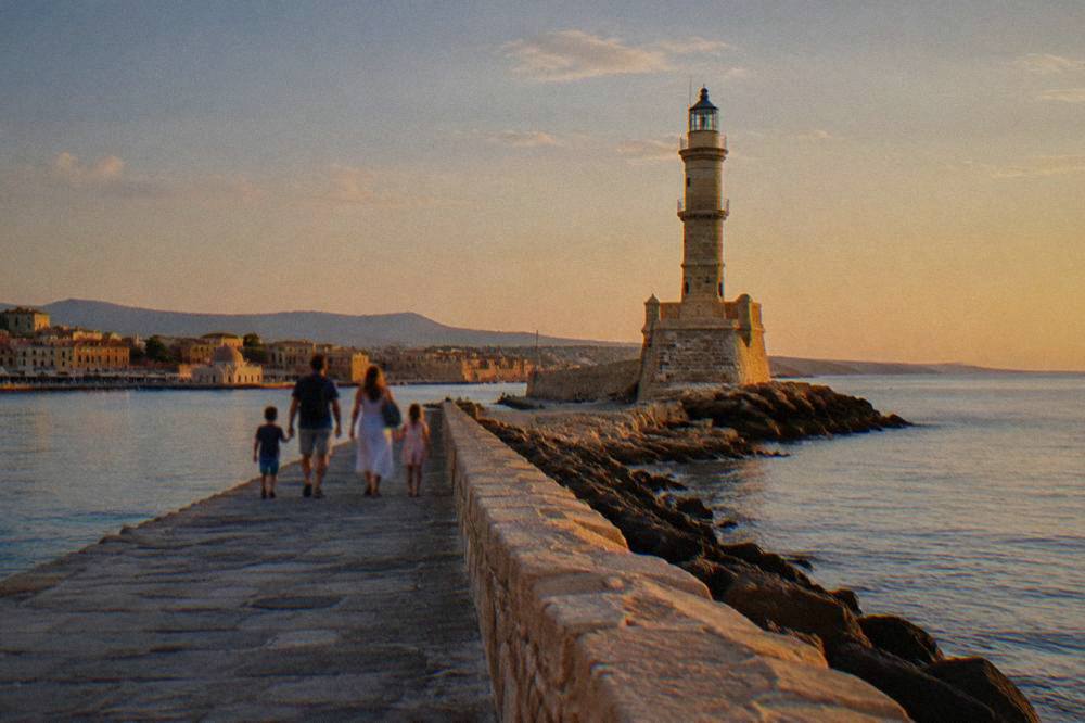 Family walking the harbour breakwater toward the Chania lighthouse on a calm morning