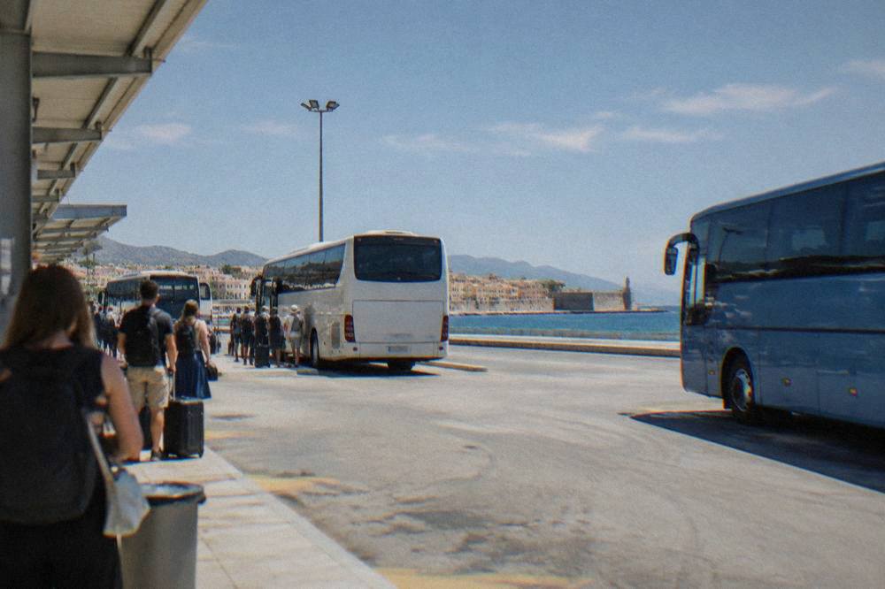 Bus station forecourt in Chania with coaches at bays and passengers waiting with bags