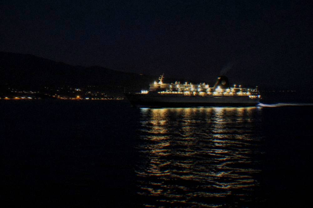 A ferry sailing across open sea at night with deck lights reflected on the water