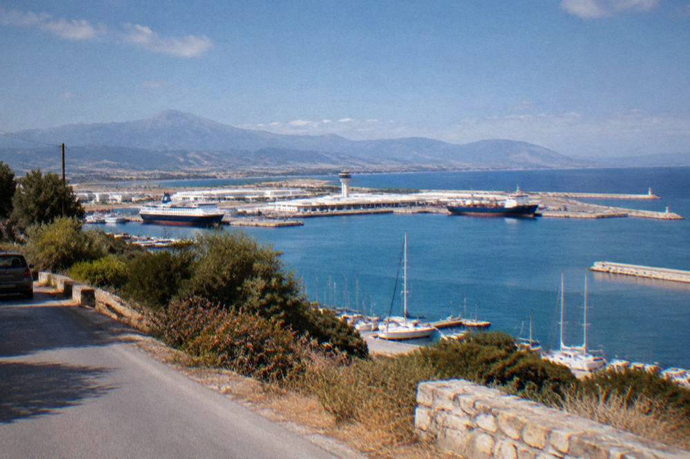 A sheltered bay with a port terminal and moored ships seen from a hillside road