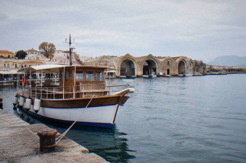 A wooden excursion boat moored in Chania harbour with the shipyard arches behind it