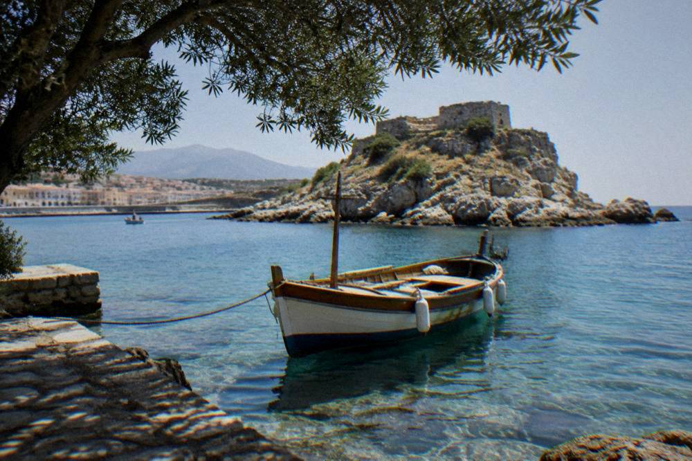 A wooden boat moored in clear shallow water beside a rocky island near Chania