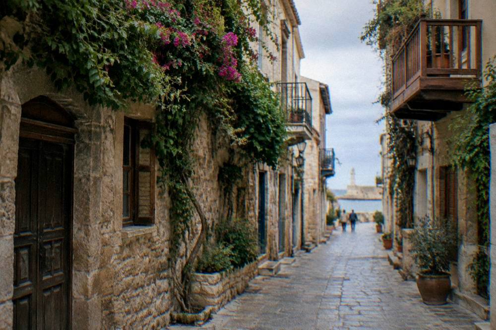 A narrow Old Town street with stone facades, wooden balconies and hanging vines in Chania
