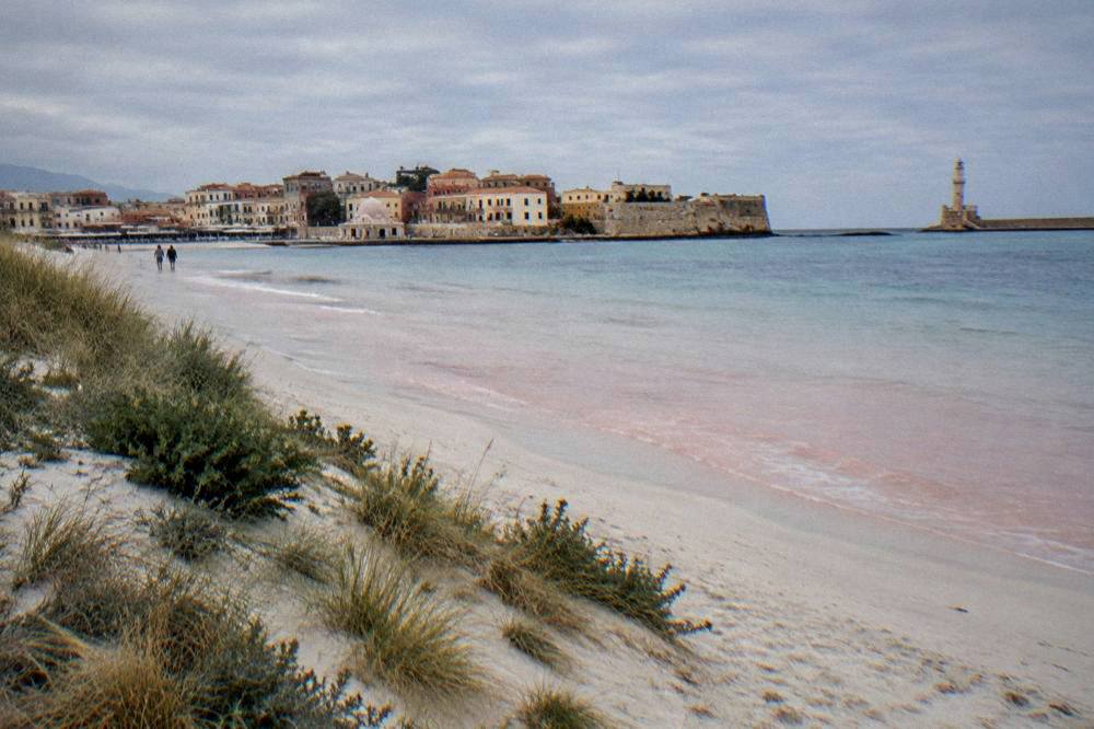 A white sand beach with shallow pink-tinged water and dunes at the south-west corner of Crete