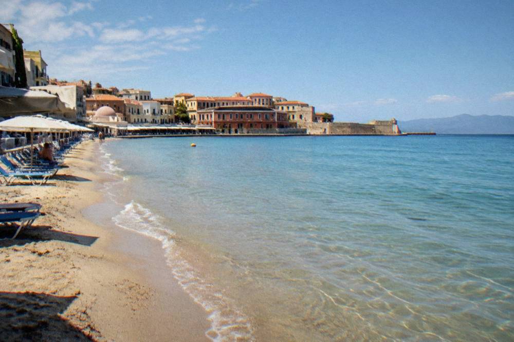 Sandy beach with calm shallow water and a few sunbeds near the city