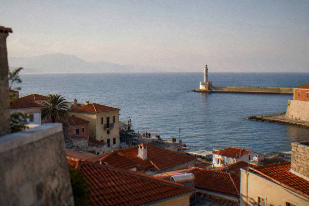 View over red-tiled rooftops toward the sea and a distant lighthouse