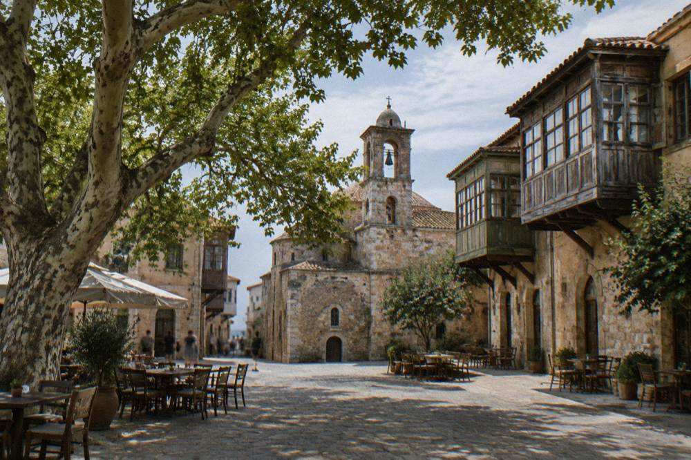 A shaded square with a plane tree, a stone church and old houses with wooden balconies in Splantzia, Chania