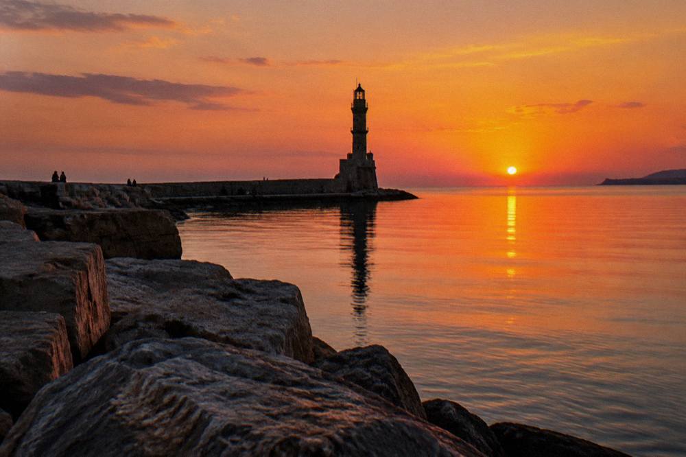 The stone lighthouse of Chania silhouetted at sunset over a glassy sea
