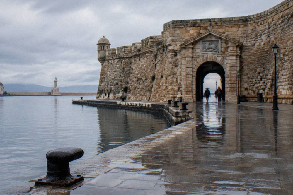 A wet stone quay beside an old fortress gateway on the Chania waterfront on a rainy day