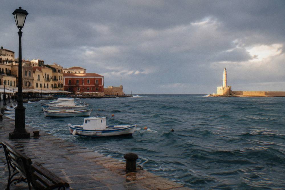 Choppy water in the Chania harbour under heavy cloud with a break of light on the far lighthouse