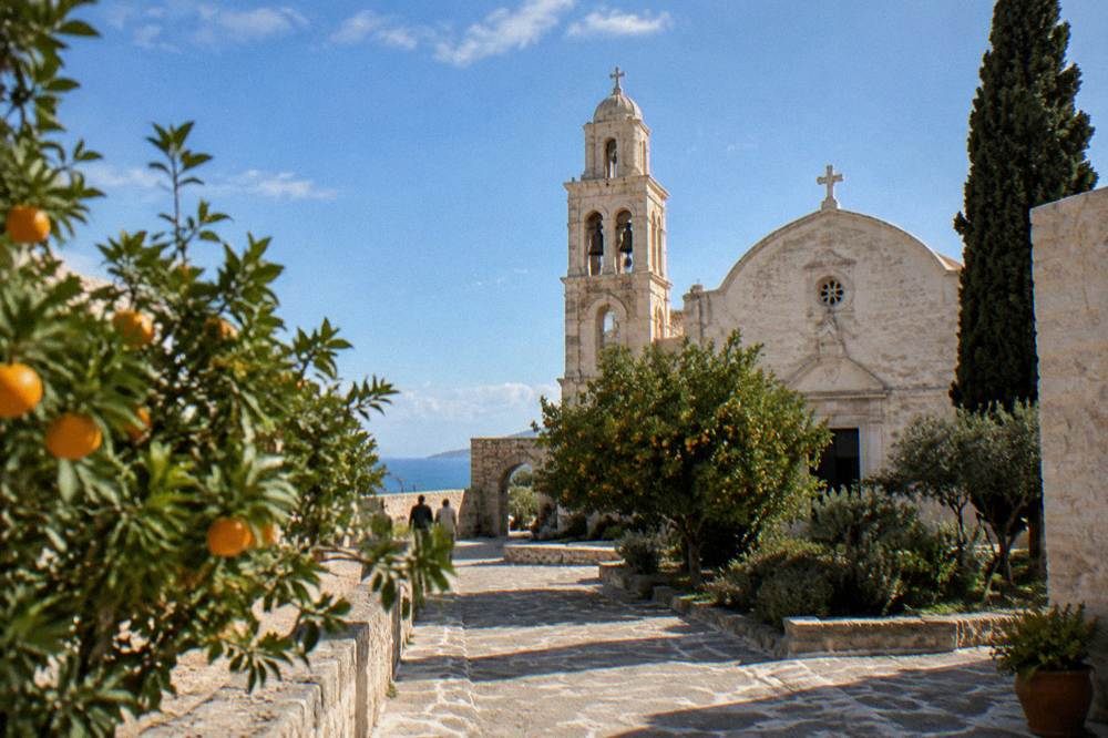 The courtyard of Agia Triada monastery near Chania with a stone church, bell tower and orange trees