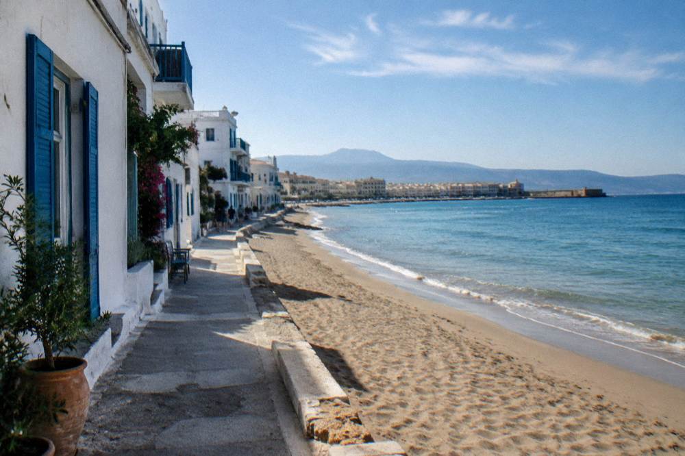 A quiet lane of whitewashed buildings with blue shutters beside the beach in Nea Chora, Chania