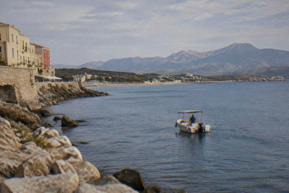 Small motorboat on calm blue water off a rocky Cretan coastline with a distant beach