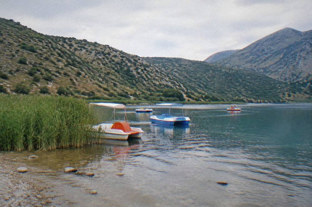 Lake Kournas ringed by hills with pedal boats near a reedy shore