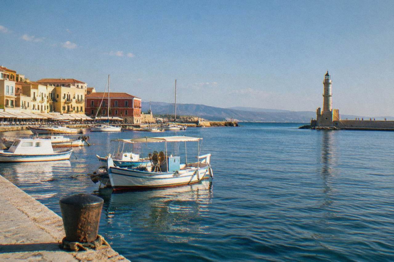 The Venetian Harbour of Chania at midday with boats, the lighthouse at the end of the mole, and harbourfront buildings