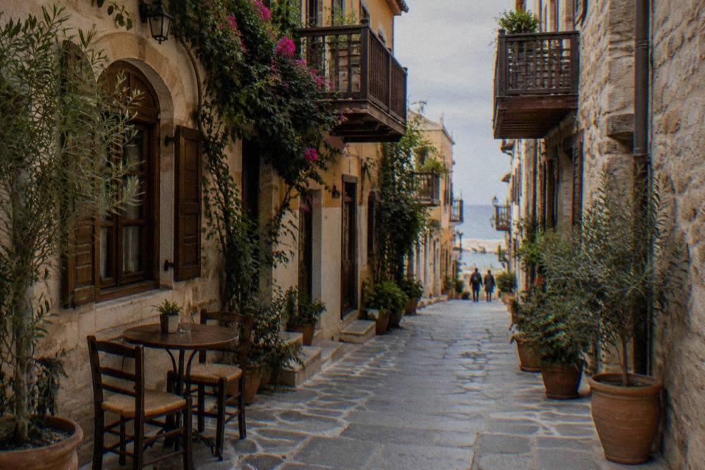 A narrow stone alley in Chania Old Town with wooden balconies, potted plants and a cafe table