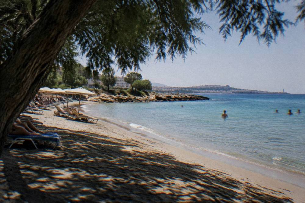 A sandy beach with shallow clear water, sunbeds and a low rocky point at Nea Chora