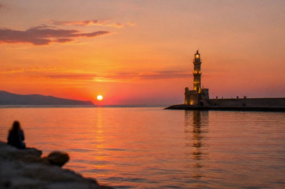 Sunset over the sea at Chania with the lit lighthouse and the harbour mole in silhouette