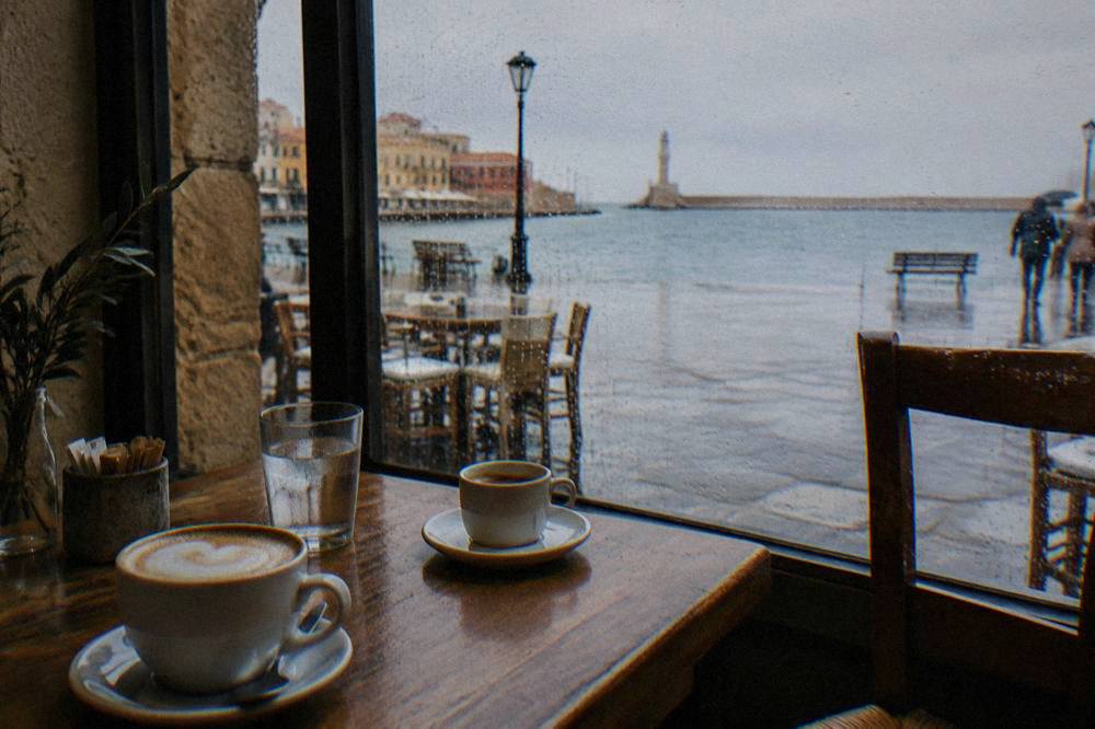Cafe interior in Chania with rain on the window and coffee cups on a wooden table