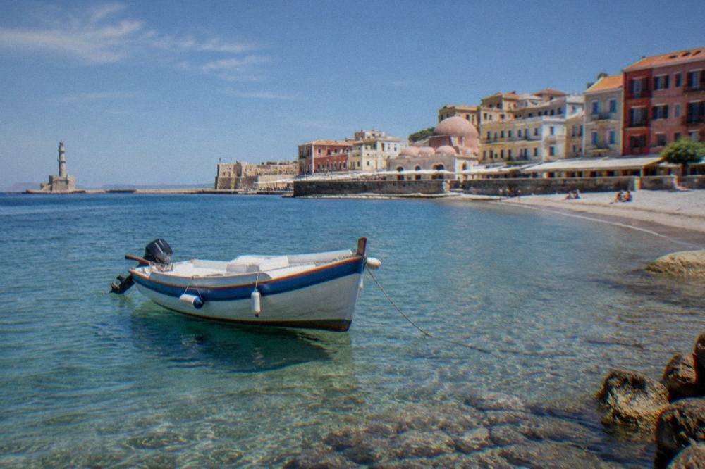 A small boat anchored in clear shallow water near a Cretan beach