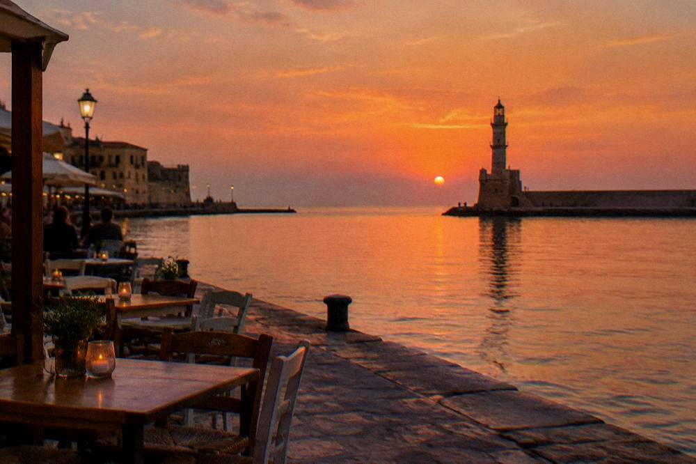 The Chania harbour front with tables and the lighthouse in the distance at dusk