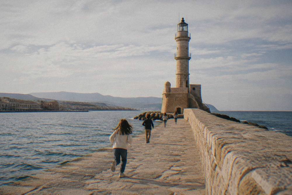 Children running on the stone harbour mole toward the lighthouse in Chania