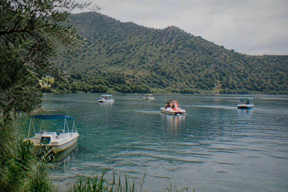 Pedal boats on the still water of Lake Kournas beneath green hills in Crete